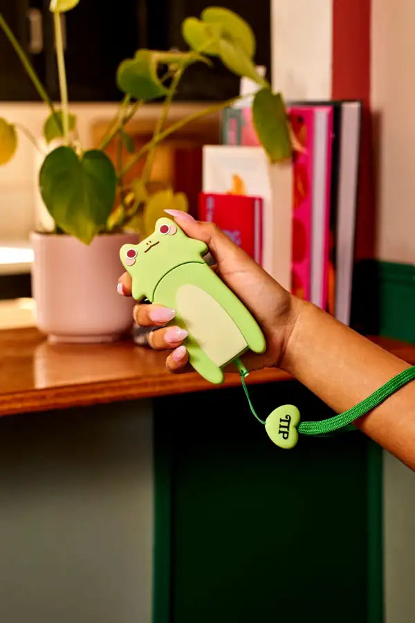 Hand holding a green stun gun with a plant and books in the background